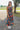 Front view of model wearing the Daydreamer Midi Dress in Hunter Green that has hunter green fabric with peach, light pink, purple, blue and olive geometric pattern, midi, smocked upper, square neck, and elastic straps.