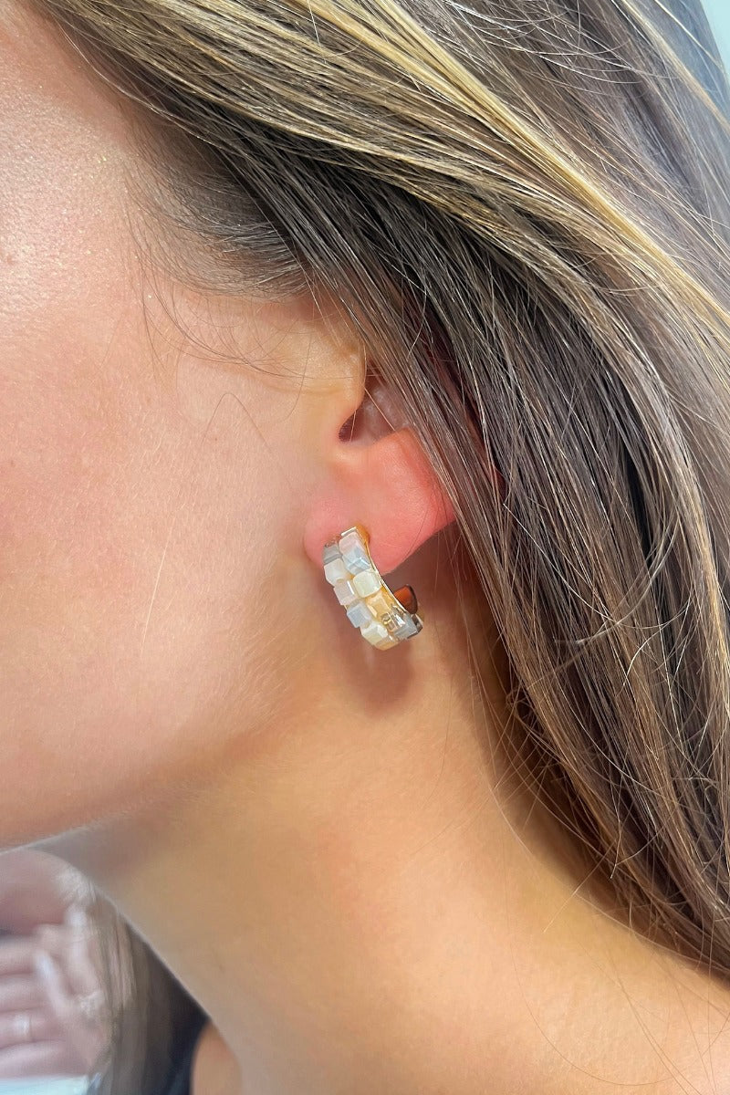 Side view of model wearing the Checkmate Earring in Natural which features grey, taupe and tan square beads, checkered design and mini open hoops with gold details.