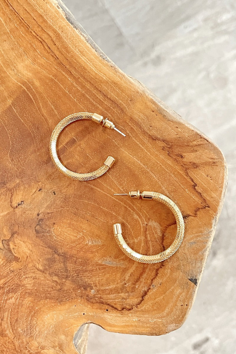 Close up view of the Herringbone Earrings which features medium, open gold hoops with monochromatic textured pattern.