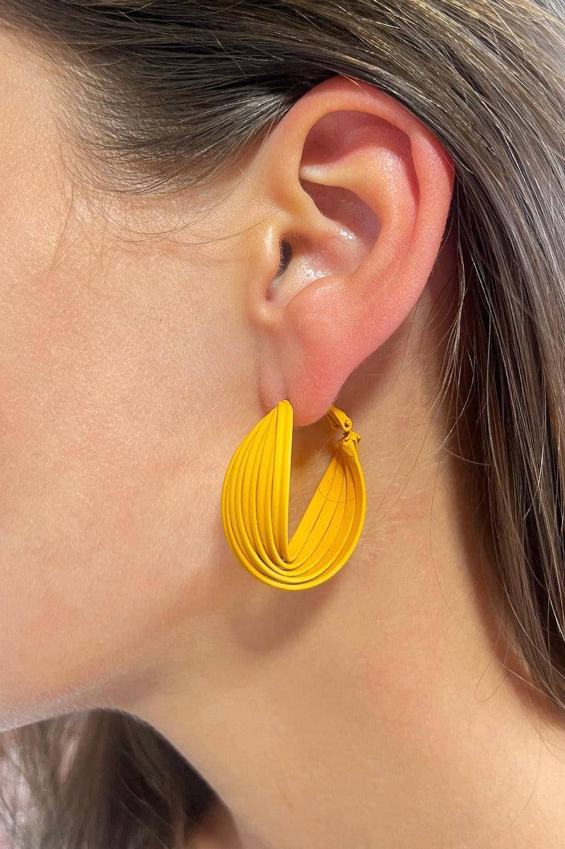Side view of model wearing the Twisted Up Earrings in Mustard which features matte mustard medium closed hoops with an intertwined design.