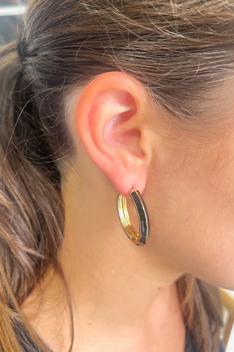 Close up view of model wearing the Blindsided Hoop Earrings which features medium, closed hoops with gold and black color-block design.