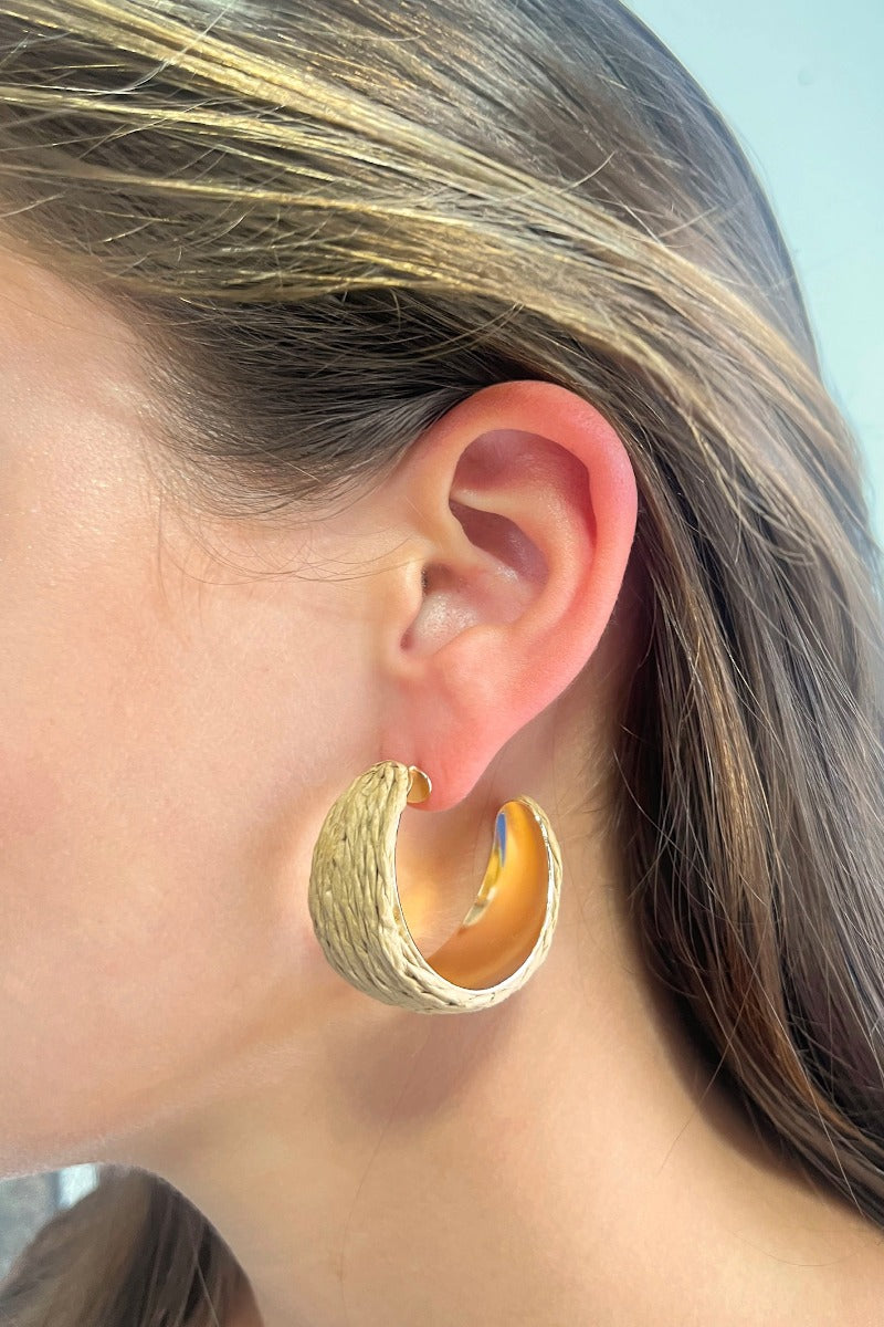 Side view of model wearing the Coast to Coast Hoop Earrings which features medium, open hoops with a natural rattan design.
