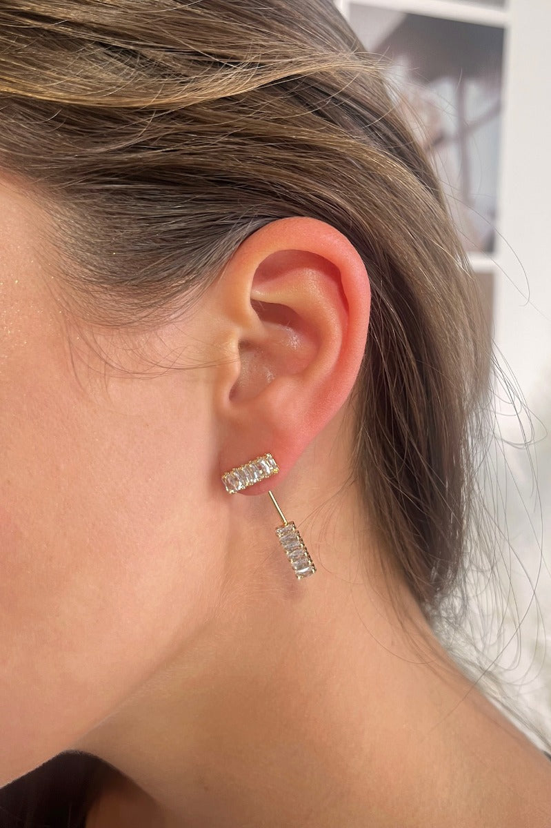 Side view of model wearing the So Easy Earrings which features cluster of clear stones linked by a gold bar with another set of clear stones.