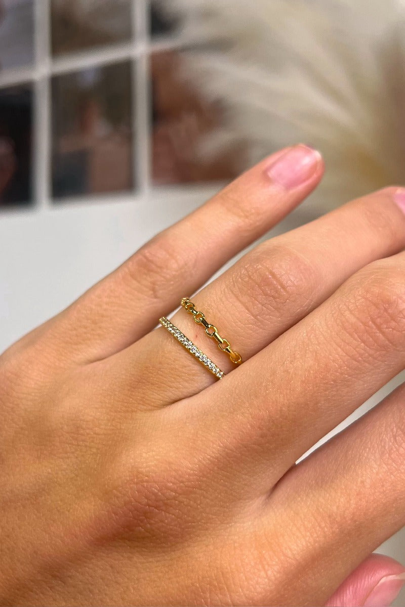 Close up view of model wearing the Loved By You Ring which features two-layered gold ring bands with chain link design and clear stones.