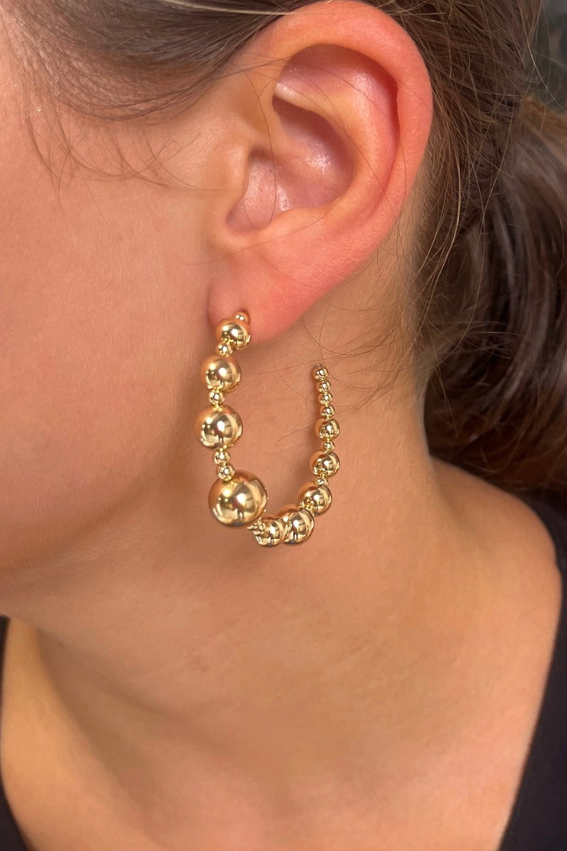 Side view of model wearing the Full Of Life Hoops in Gold which features large, open gold hoops with small and large gold beads.
