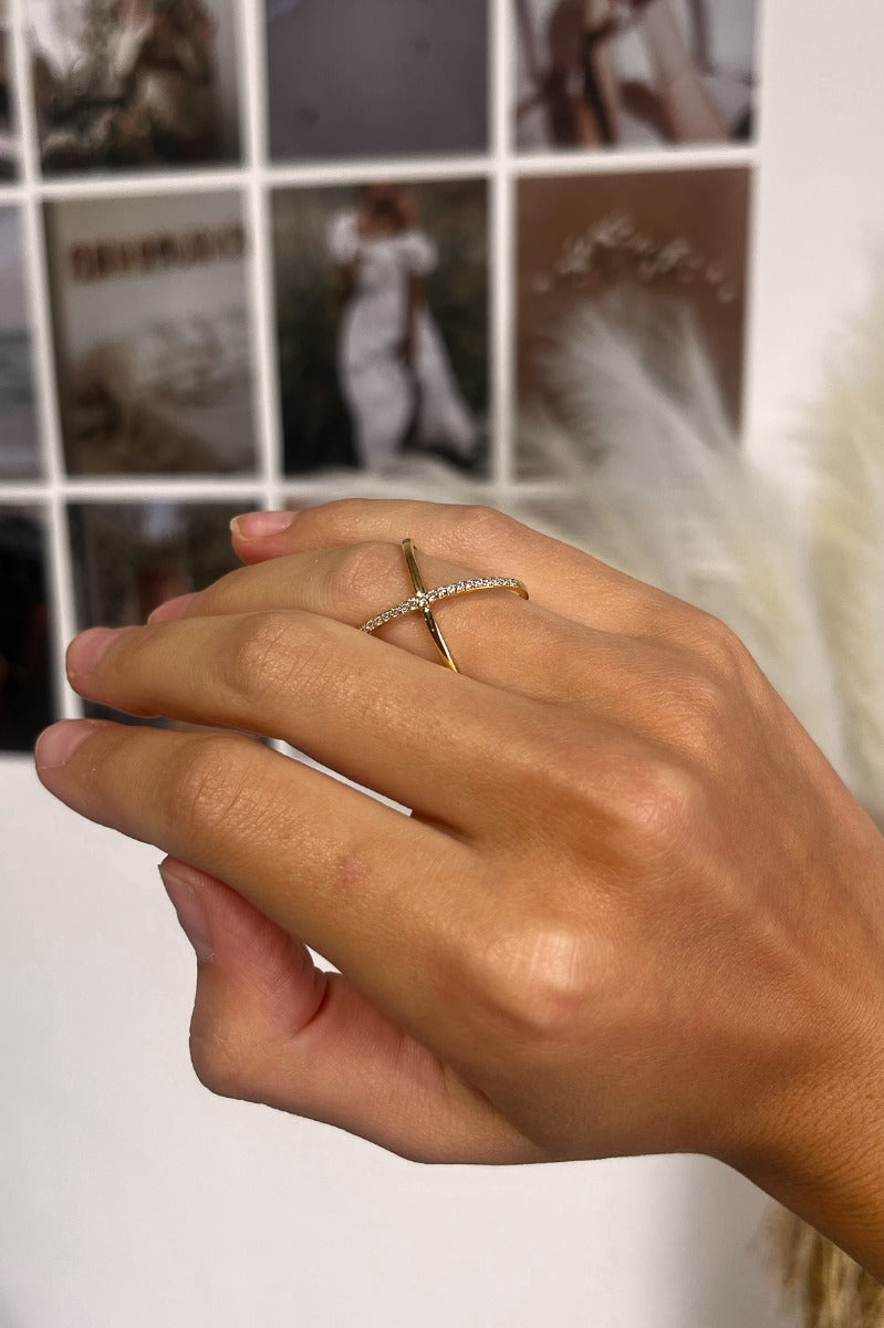 Close up view of model wearing the Cross My Heart Ring which features two gold, crossed bands with clear stones.