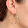 Side view of model wearing the Nothing On You Earrings which features medium, open hoops with hammered scalloped design.