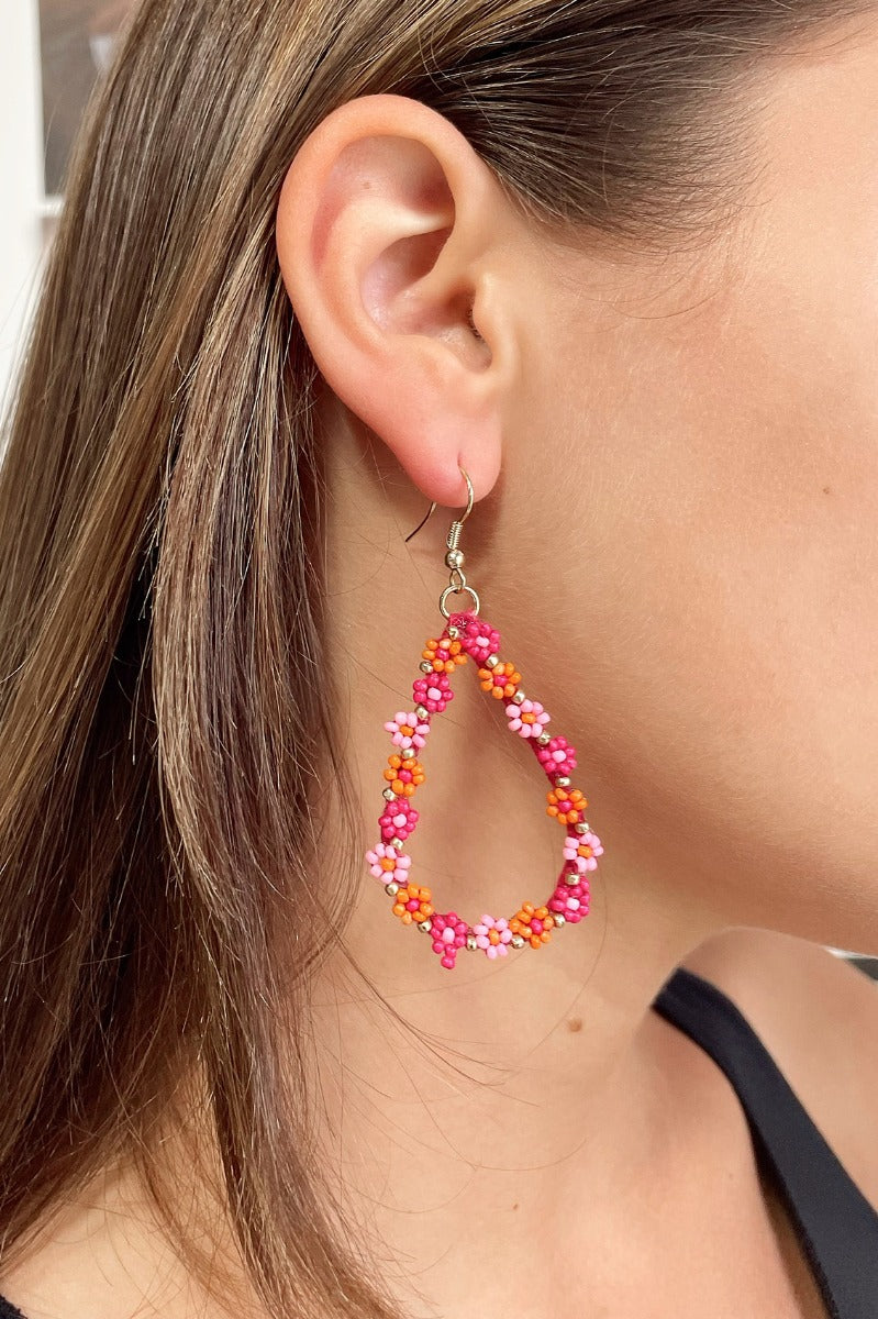 Side view of model wearing the Flower Power Earrings in Multi which features teardrop shaped hoop covered with orange, hot pink and light pink flowers.