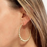 Side view of model wearing the In The Magic Earrings in Gold which features open, large hoops covered with gold small and large beads.