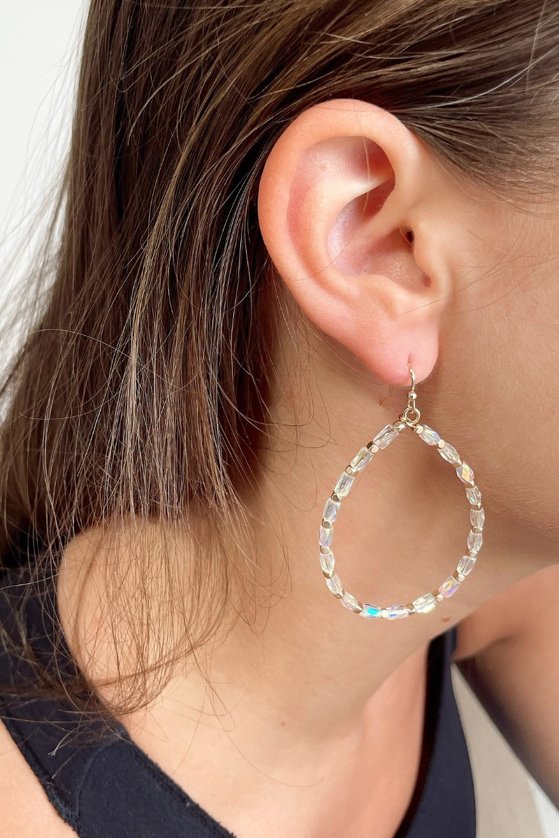Side view of model wearing the Enchanted By You Earrings which features teardrop shaped hoops with iridescent and gold beads.