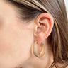 Side view of model wearing the Krista Hoop Earrings which features scooped, closed hoops with monochromatic speckled design.