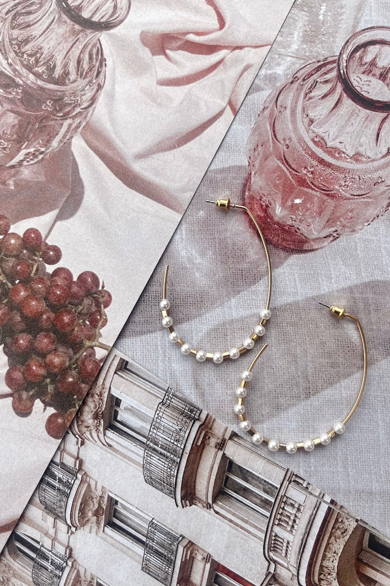 Flat lay view of Think Of Me Pearl Hoops which features open-shaped gold hoops with pearls and gold beads.