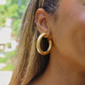 Front view of model wearing the Fearless Dreams Gold Hoop which features gold shimmer, medium size, open hoops.