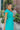 Side view of model wearing the Cabana Bay Midi Dress which features turquoise fabric, midi length, a tie around the waist, turquoise lining, one shoulder ruffle strap, and a monochromatic side zipper with a hook closure.