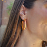 Front view of model wearing the Sunset Daze Earring which features open medium size orange hoops with iridescent shimmer.