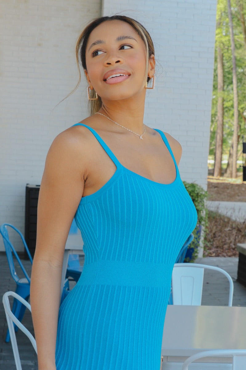 Close side view of model wearing the Coastal Paradise Dress that has cobalt blue ribbed fabric, midi length, a round neckline, an elastic waistband, and spaghetti straps