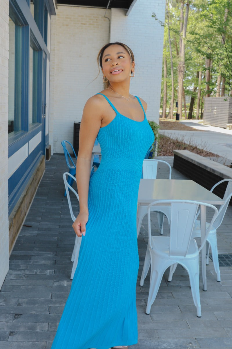 Full body side view of model wearing the Coastal Paradise Dress that has cobalt blue ribbed fabric, midi length, a round neckline, an elastic waistband, and spaghetti straps
