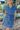 Close front view of model wearing the East Side Denim Dress that has dark wash denim fabric, mini length, pockets, a silver button up front, a collared neck, a tie around the waist, and short sleeves.