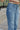 Close up side view of model wearing the Rooted Denim: Breaking Rules Cropped Flare which features medium denim wash fabric, cropped flare leg, front zipper with button closure, two front pockets, two back pockets, belt loops and distressed details.