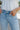Close up view of model wearing the Rooted Denim: Next Level Confidence Jeans which features medium wash denim fabric, straight legs, two front pockets, two back pockets, a front zipper with a button closure, belt loops and a frayed hem.