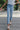 Front view of model wearing the Rooted Denim: Next Level Confidence Jeans which features medium wash denim fabric, straight legs, two front pockets, two back pockets, a front zipper with a button closure, belt loops and a frayed hem.