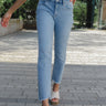 Front view of model wearing the Rooted Denim: Next Level Confidence Jeans which features medium wash denim fabric, straight legs, two front pockets, two back pockets, a front zipper with a button closure, belt loops and a frayed hem.