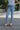 Front view of model wearing the Rooted Denim: Next Level Confidence Jeans which features medium wash denim fabric, straight legs, two front pockets, two back pockets, a front zipper with a button closure, belt loops and a frayed hem.