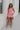 Full body front view of model wearing the I'm Smitten Dress in Pink that has pink ruched mesh fabric, pink lining, a strapless wire v-neck, and a back zipper and hook closure