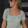 Front view of model wearing the Lucky One Top that has light sage textured fabric, a cropped waist, an elastic band, ruffle details, a square neckline, and short sleeves