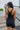 Back view of model wearing the Comfort Zone Lightweight Romper which features stretchy black fabric, a scooped neckline, a racerback, a built in bra, and fitted shorts.