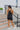 Full body back view of model wearing the Comfort Zone Lightweight Romper which features stretchy black fabric, a scooped neckline, a racerback, a built in bra, and fitted shorts.