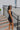 Side view of model wearing the Comfort Zone Lightweight Romper which features stretchy black fabric, a scooped neckline, a racerback, a built in bra, and fitted shorts.