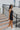 Full body side view of model wearing the Comfort Zone Lightweight Romper which features stretchy black fabric, a scooped neckline, a racerback, a built in bra, and fitted shorts.