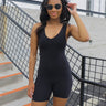 Front view of model wearing the Comfort Zone Lightweight Romper which features stretchy black fabric, a scooped neckline, a racerback, a built in bra, and fitted shorts.