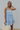 Front view of model wearing the Now Or Never Dress which features light blue textured fabric, a ruffle two-tiered mini-length body, light blue lining, a square neckline, and thick straps.