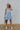 Full body view of model wearing the Now Or Never Dress which features light blue textured fabric, a ruffle two-tiered mini-length body, light blue lining, a square neckline, and thick straps.