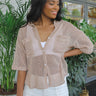 Front view of model wearing the Coastal Dreams Top which features taupe open knit fabric, a scooped hem, pearlescent buttons, a collared neckline, two front chest pockets, and short sleeves.