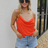 Front view of model wearing the Taste Of The Sun Tank which features red orange fabric, a cowl neckline, red orange lining, and adjustable spaghetti straps.