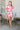 Full front view of model wearing the Nothing Compares Floral Dress that has white brocade fabric with a fuchsia and red floral print, a round neck, short puff sleeves, an open back, and a back zipper.