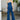 Full front view of model wearing the Daisy Jones Jumpsuit that has dark wash denim fabric, a thick waistband, a strapless sweetheart neck, a smocked back, a side zipper, and flared pant legs
