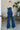 Full front view of model wearing the Daisy Jones Jumpsuit that has dark wash denim fabric, a thick waistband, a strapless sweetheart neck, a smocked back, a side zipper, and flared pant legs