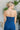 Upper back view of model wearing the Daisy Jones Jumpsuit that has dark wash denim fabric, a thick waistband, a strapless sweetheart neck, a smocked back, a side zipper, and flared pant legs
