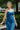 Upper front view of model wearing the Daisy Jones Jumpsuit that has dark wash denim fabric, a thick waistband, a strapless sweetheart neck, a smocked back, a side zipper, and flared pant legs