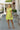 Full body front view of model wearing the Brighter Days Ahead Dress that has lime green fabric, a three-tiered body style,, a smocked elastic waist, tie details, a v neck with ruffles, and short sleeves