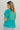 Back view of model wearing the Float On Floral Top that has teal fabric, a monochromatic stitched floral and eyelet pattern, a peplum body, teal lining, a v-neckline, and short puff sleeves with cuffs