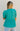 Back view of model wearing the Float On Floral Top that has teal fabric, a monochromatic stitched floral and eyelet pattern, a peplum body, teal lining, a v-neckline, and short puff sleeves with cuffs