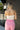 Upper back view of model wearing the Pretty in Pink Pants that have pink fabric, a hidden front zipper with a hook closure, belt loops, an elastic waistband in the back, pockets on each side, and wide legs
