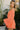 Side view of model wearing the Take Me To The Tropics Romper that has coral fabric, an elastic waist, a tie around the waist, an off-the-shoulder neck, and 3/4 flare sleeves with ruffle trim.