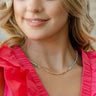 Close up of model wearing the Need A Vacation Necklace that has a gold chain link covered in iridescent, pink purple, blue, gold and green beads.