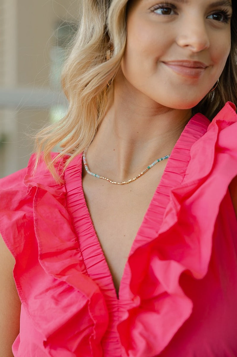 Image of model wearing the Need A Vacation Necklace that has a gold chain link covered in iridescent, pink purple, blue, gold and green beads.